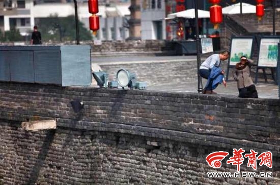 男子站城墙上扶灯柱拍照 旅游不是耍杂技