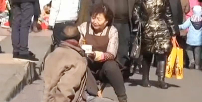 大妈蹲地给乞讨男子喂面
